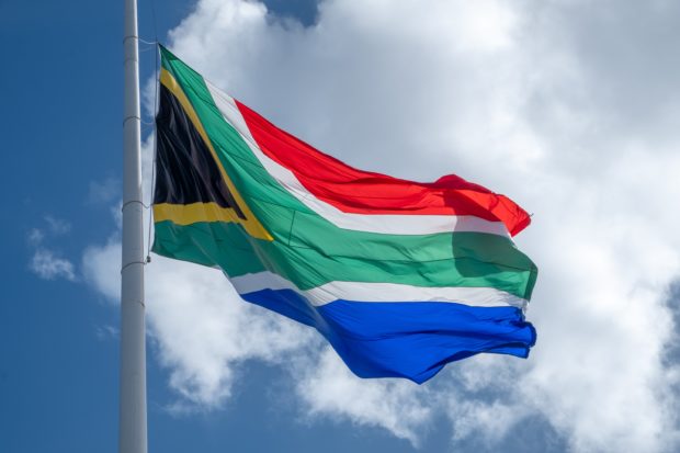South African flag blowing in the breeze with a blue sky and clouds in the background. 