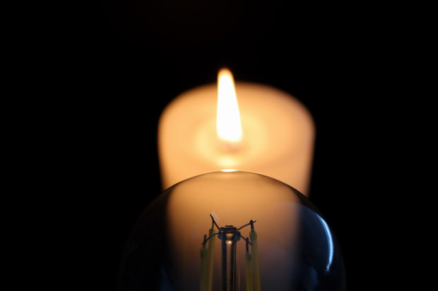 Lit candle behind an unlit lightbulb during an electricity blackout. 