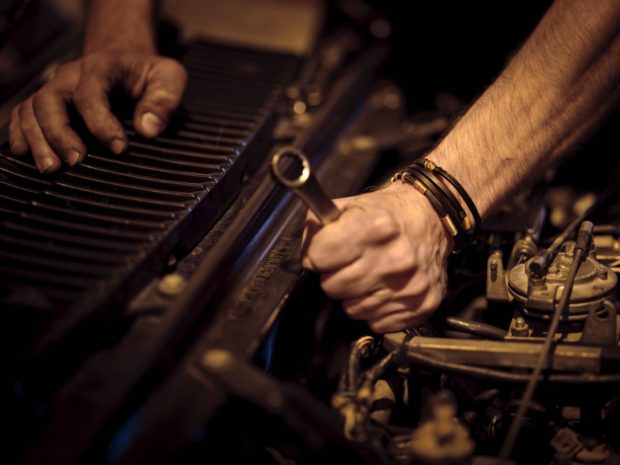 Close-up of white male hands in the process of fixing a car engine. Moody lighting.