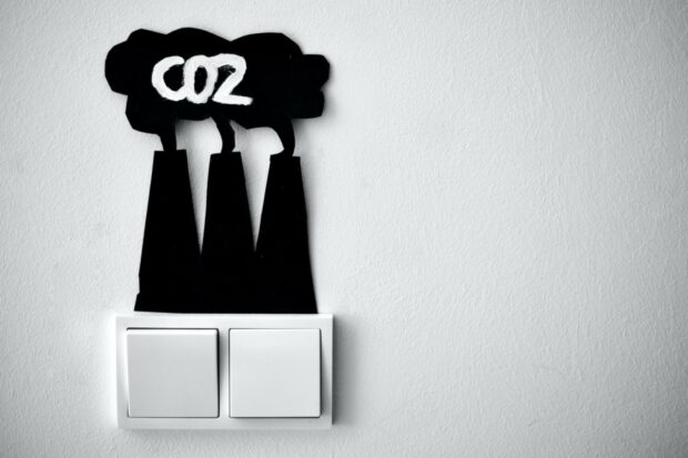 Graphic intended to show the link between power and carbon dioxide. It shows two electric light switches and above them is a (presumably card, maybe plastic) cut-out in the shape of power station chimneys with a cloud above them. On the cloud is written "CO2". 