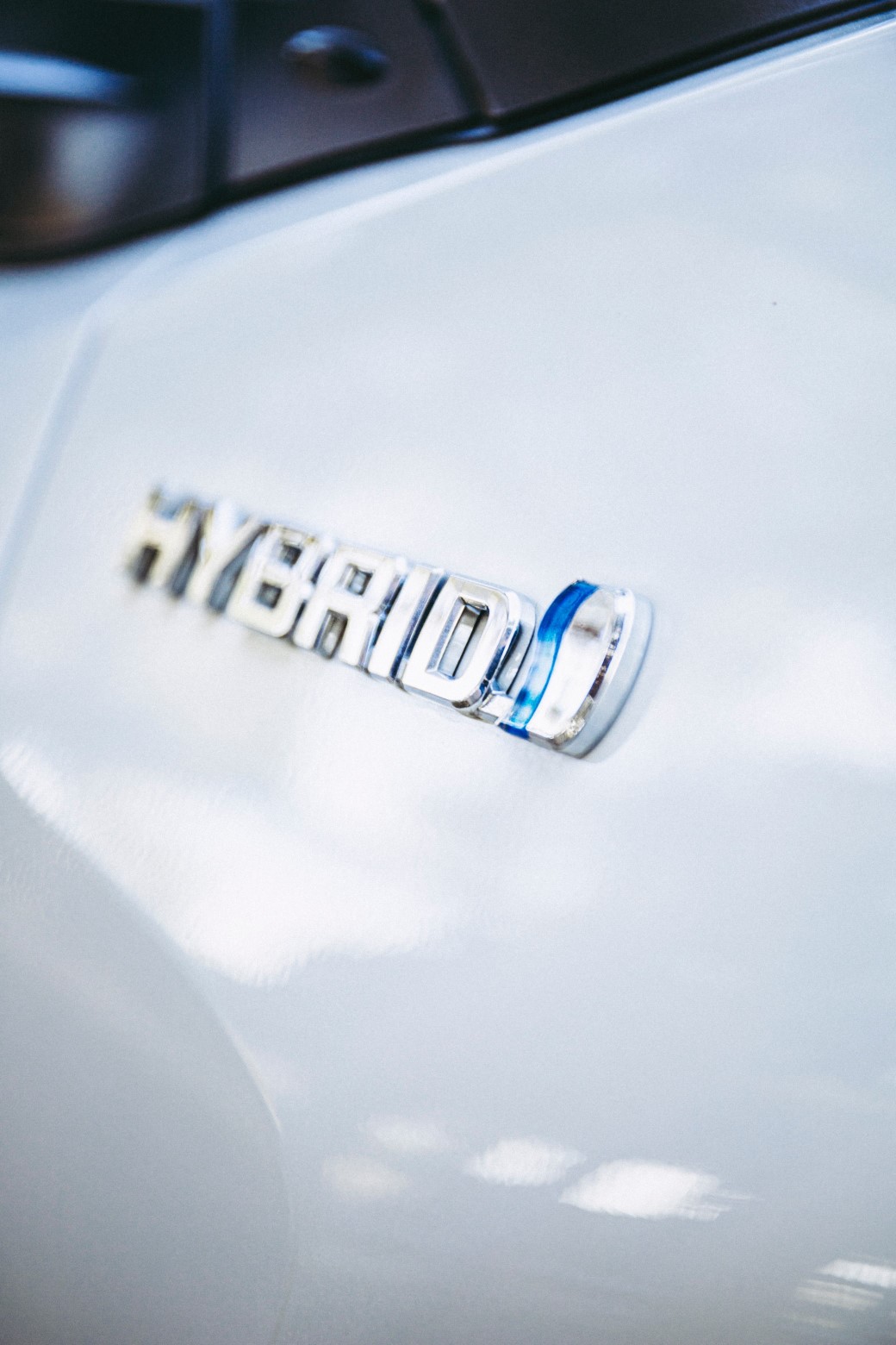 Close-up of the side of a shiny white car. It has silver lettering on it spelling out the word "HYBRID".